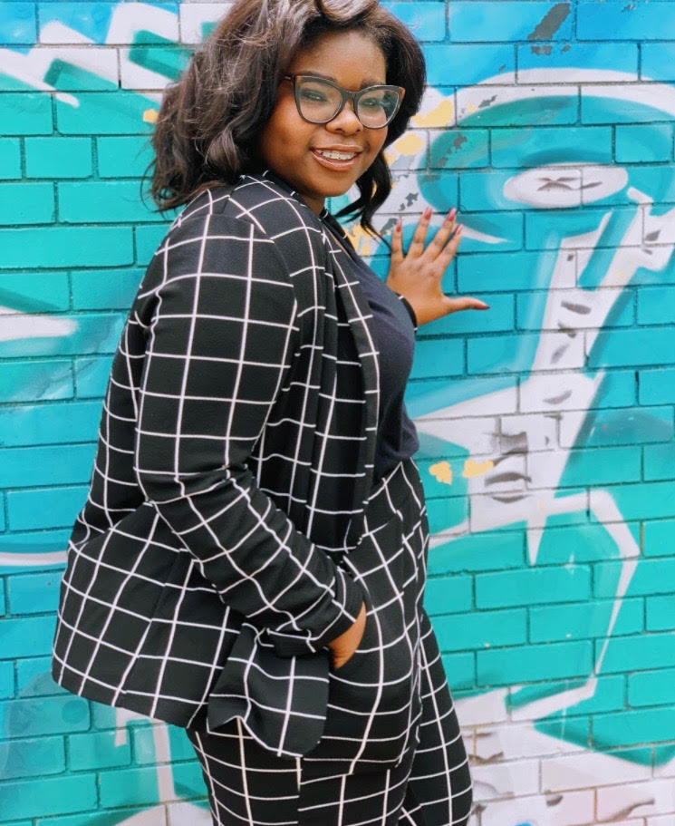 female student standing at colorful wall, wearing glasses and a suit